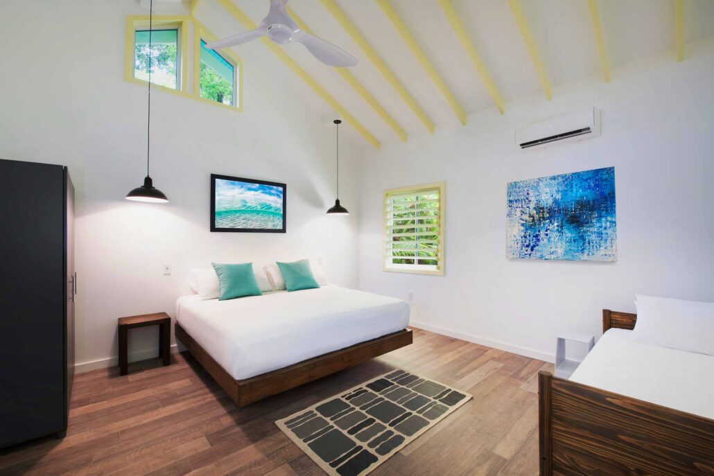 Modern interior of a Garden Casita at Puerta Azul Roatan featuring a king bed, high vaulted ceilings with yellow beams, and bright tropical decor.