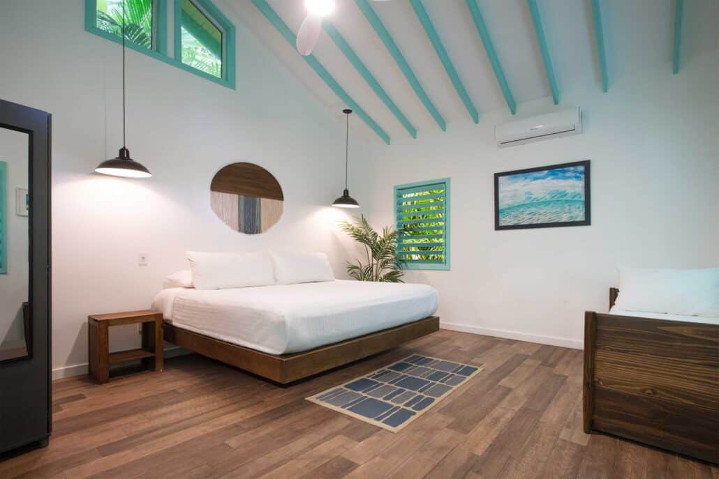Interior of the Family Garden Villa at Puerta Azul Roatan featuring a king bed, twin bed, turquoise vaulted ceilings, and a kitchenette.