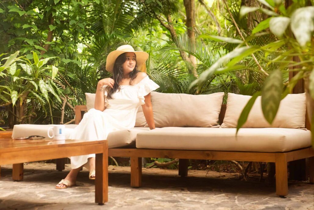 A guest in a sun hat relaxing on a comfortable outdoor sofa in the lush garden lounge at Puerta Azul Roatan.