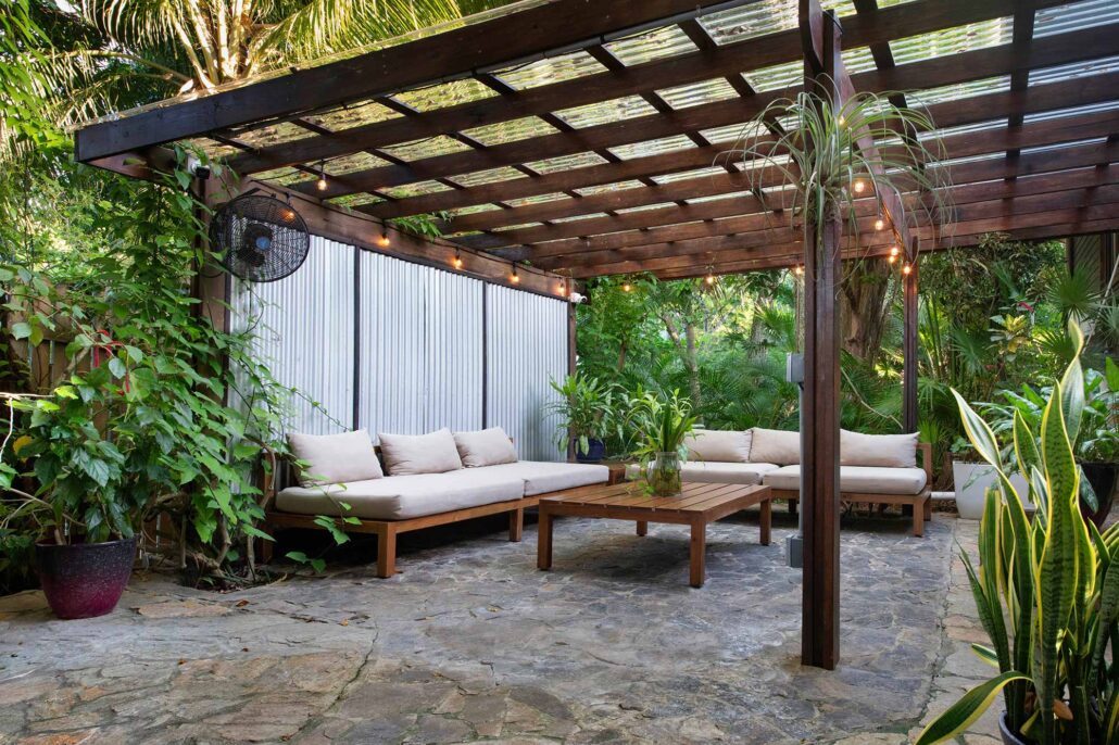 Al fresco breakfast and lounge area at Puerta Azul Roatan, featuring comfortable seating under a wooden pergola and lush tropical greenery.