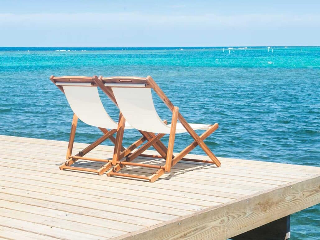 Two white and wood sling lounge chairs sitting on a private wooden dock overlooking the bright turquoise Caribbean Sea in Roatan.