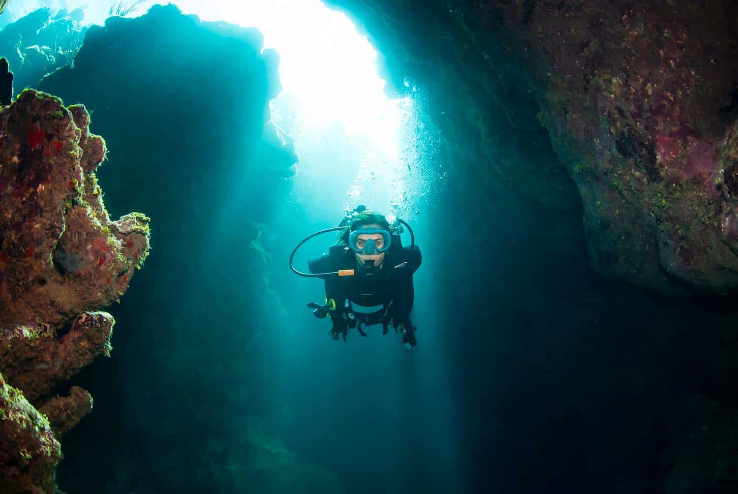 Subacqueo che esplora l'interno del canyon sottomarino Spooky Channel a Roatan con fasci di luce solare.