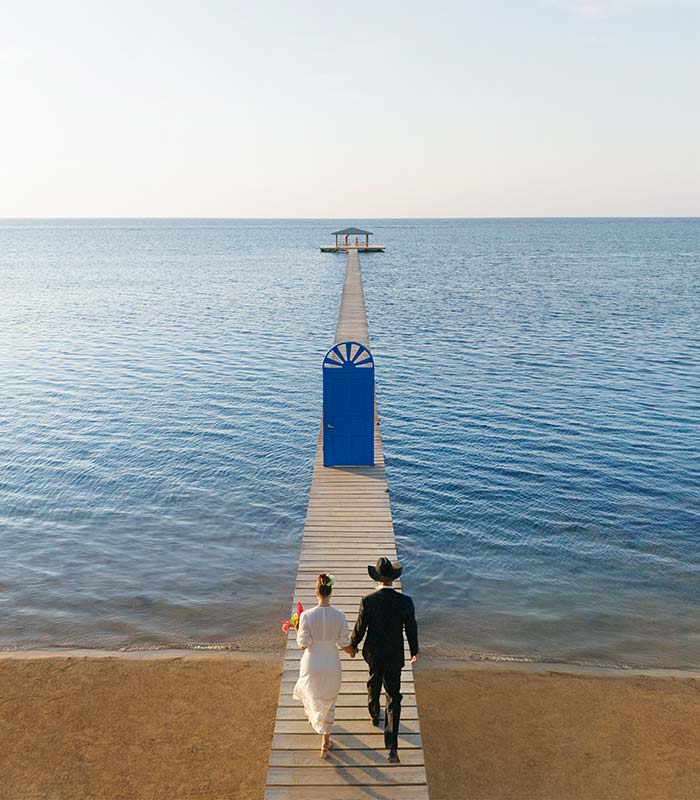 Bride and groom walking on the overwater wooden dock for the Package One ceremony setup at Puerta Azul Roatan