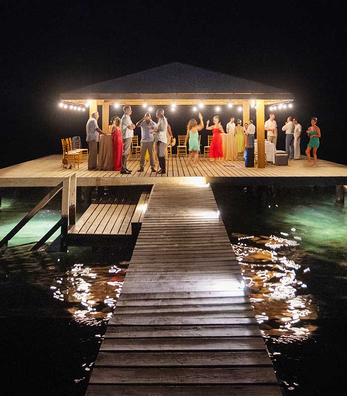 Wedding guests dancing and celebrating during a night reception at the private overwater palapa dock in Puerta Azul Roatan