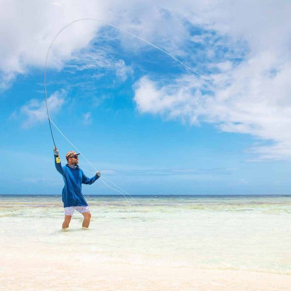 A man casting a fly fishing rod while wading in the shallow, clear salt flats of Roatan near Puerta Azul.