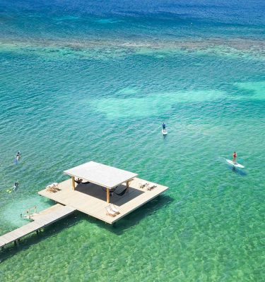 Aerial view of guests snorkeling and paddleboarding in turquoise water at the end of the private 400-foot dock at Puerta Azul Roatan.