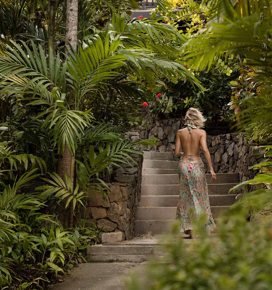 A woman walking up stone stairs surrounded by lush tropical palm trees and greenery at Puerta Azul Roatan hotel.