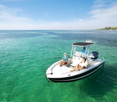 Guests relaxing on the bow of a private white motorboat over crystal-clear turquoise water during an island excursion at Puerta Azul Roatan.